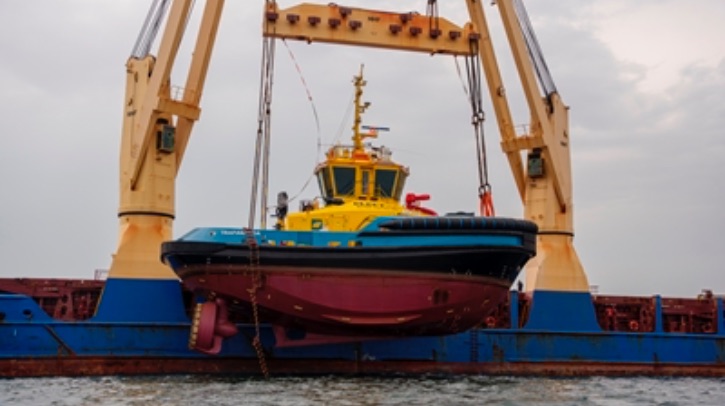 Latin America’s first fully electric tug sets off for delivery A yellow, blue and red electric tug is lowered into the water.