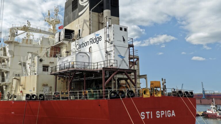 Carbon Ridge announces shipping’s first centrifugal carbon capture system The Carbon Ridge STI Spiga pictured in port. it has a red base and white buildings on top, with other small boats in the background in the port