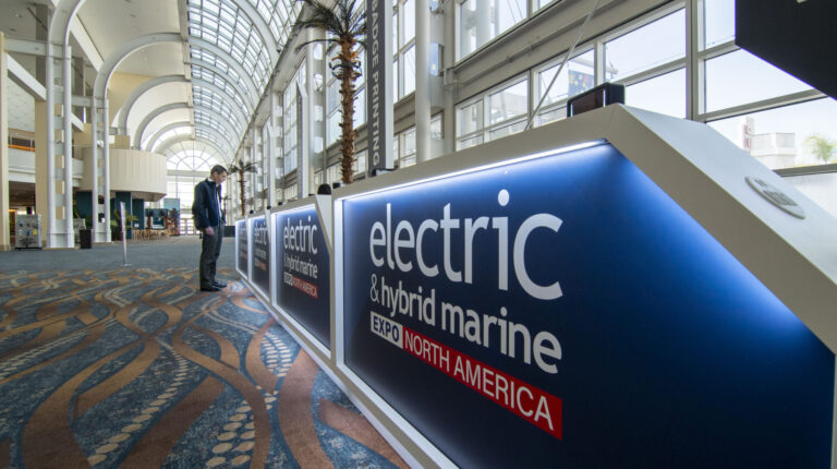 A man stands at the entrance desk to the Electric & Hybrid Marine Expo North America, with the exp branding on display and the convention centre lobby stretching out in the background