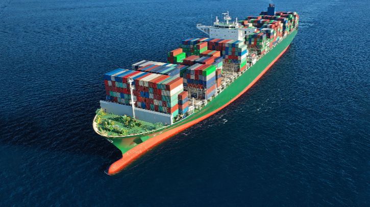 A green and orange ship carrying containers of various colours sails across the ocean
